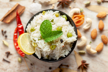 Close-up of Indian Basmati steamed Rice or matar (Pea) pulao or Pulav garnished with fresh green mint leaf in a black bowl.