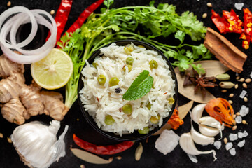 Close-up of Indian Basmati steamed Rice or matar (Pea) pulao or Pulav garnished with fresh green mint leaf in a black bowl.