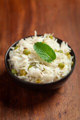 Close-up of Indian Basmati steamed Rice or matar (Pea) pulao or Pulav garnished with fresh green mint leaf in a black bowl.