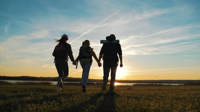 Happy family are running on hike trip. Teamwork family hiking in nature. Parents with child hiking adventure. Group of people run the field at sunset. Friendly family summer vacation together.
