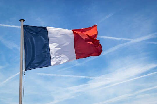 French flag on flagpole flutters in the wind against blue sky.