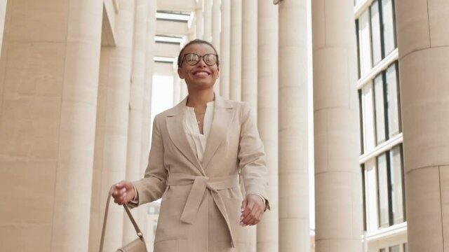 Low-angle Tracking Medium Slowmo Shot Of Young Confident Businesswoman With Beautiful Smile Walking In City Downtown Going To Or From Work Looking Around