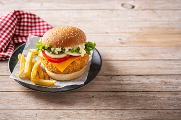 Crispy chicken burger with cheese and french fries on wooden table. Copy space