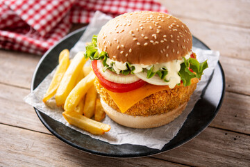 Crispy chicken burger with cheese and french fries on wooden table