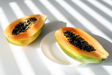 Papaya on a plate on a white table. Bright sunlight through the blinds. Contrasting shadows.