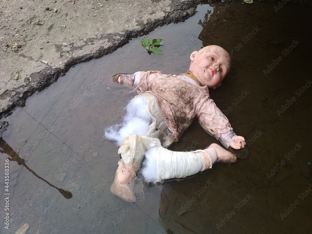 Wall mural a torn, broken baby doll in a puddle.