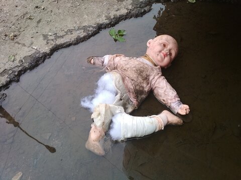 a torn, broken baby doll in a puddle.