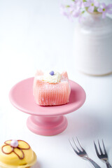 Yellow pink petit fours on a lilac cake stand. Vase with lilac flowers