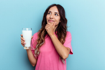Young mixed race woman holding a glass of milk isolated on blue background looking sideways with doubtful and skeptical expression.
