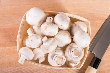 White champignons in a basket and a knife on the table, top view, close-up