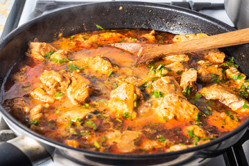 Cooking homemade chicken curry in a skillet on a gas stove, close-up