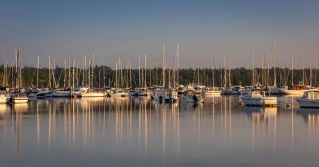 Fotobehang A marina of sailing boats at sunrise with numerous reflections of their masts all on the Beaulieu River at Buckler's Hard, Hampshire UK © Andrew