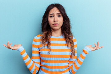 Young mexican woman isolated on blue background doubting and shrugging shoulders in questioning...