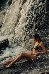 Woman sits under the waterfall and enjoys the falling water.