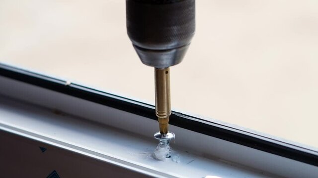 Manufacture of plastic windows and doors. Worker fastens the fittings with a screwdriver to the plastic window in the shop for the production of plastic and metal windows and doors. Screwing screws. 