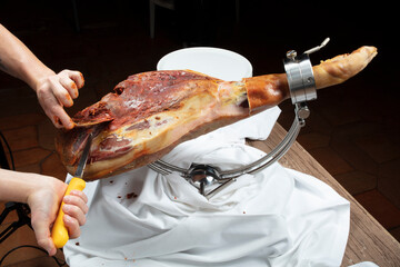 Manos cortando un jamón serrano ibérico de bellota con cuchillo. Hands cutting an acorn-fed...