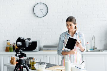 culinary blogger showing digital tablet with blank screen during online cooking near digital camera.
