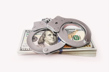 Steel handcuffs and one hundred dollar bills on a white background.