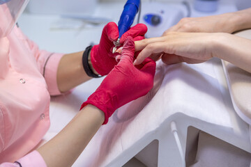 A woman sits at a table and gives a manicure to client.Nail clipper.A manicure master in a pink robe, a protective screen and a mask.Personal protective equipment of the beauty master.Women's manicure