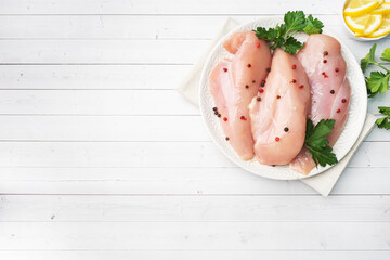 Raw chicken breast fillet on a plate, white wooden background. top view, copy space