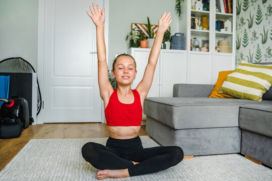 A cheerful little girl does yoga on the carpet at home, doing fitness exercises at home. Home remote fitness.