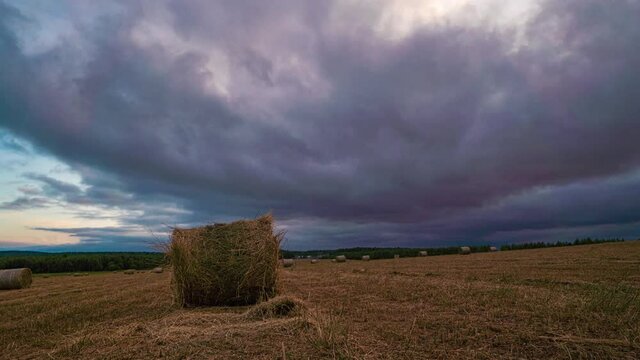 4K UHD flat hill meadow timelapse at the summer sunset time. Wild nature and rural haystacks on grass field. Sun rays and green trees. Motorised dolly slider