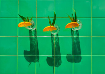 Refreshing lemonade drink in crystal glasses leaves orange slice on green tile background shadows....