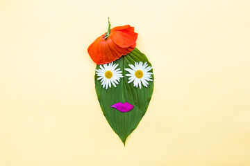 Fashionable female face made of a green leaf, with daisy eyes and a poppy flower cap. Woman care cosmetics with natural ingredients