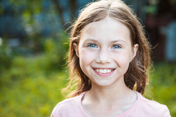 Portrait of attractive caucasian little student girl with beautiful blue eyes. Happy smiling child looking at camera - close-up, outdoors