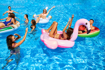 Friends having party in private holiday villa swimming pool. Happy young people swim on inflatable...
