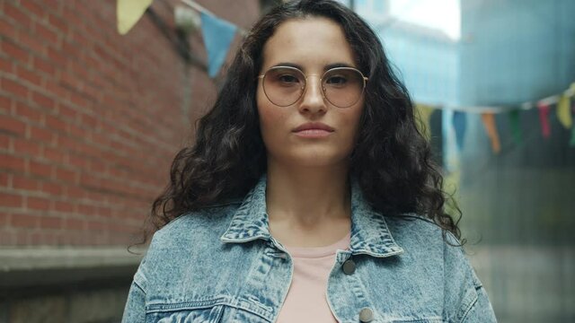 Portrait of serious mixed race woman wearing stylish glasses standing outside on urban background looking at camera. Youth and expressions concept.