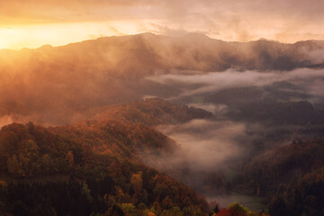 Fototapeta na wymiar Scenic view of wooded Alps mountains at sunrise, amazing autumn landscape with mountain ridge, colorful trees, morning mist and cloudy sky, Jamnik, Slovenia. Outdoor travel background
