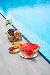 Breakfast by the pool. Watermelon, berries, croissants, non-alcoholic cocktails by the pool. Vertical photography.