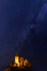 Fototapeta na wymiar Scenic view of illuminated Jamnik church St Primus and Felician on the hill at night, Slovenia. Beautiful landscape with blue starry sky, outdoor travel background, famous tourist attraction