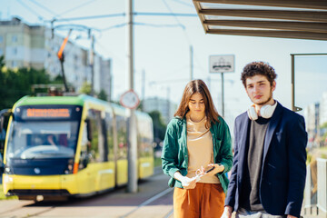 Outdoor shot of attractive tired millennial couple dressed casual wanders around city, enjoys leisure time with tram on background. People, public transportation concept.