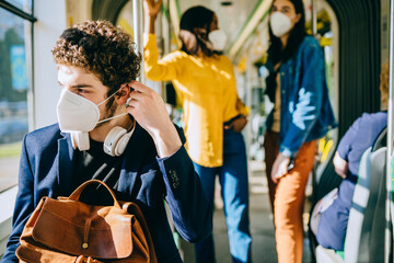 Curly caucasian man puts on a face medical mask while traveling inside public transport, tram,...