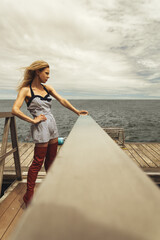 Attractive young blonde woman with crimped hair, wearing a striped dress and long red boots, on the dock of a lobster fisherman's cove