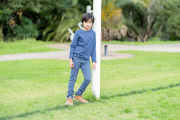 Portrait of lonely child. Young boy standing in park leaning against pole looking towards camera. Shot in natural light. 