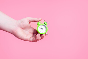 male hand holding alarm clock on pink background