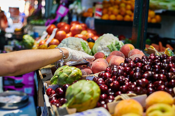 Customer in the market picking fruit from a box with gloves