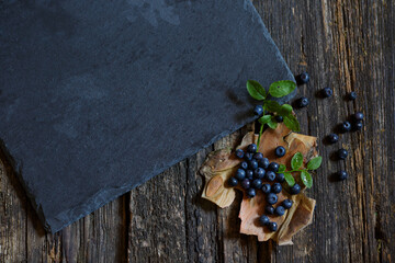 Fresh blueberries with green leaves and water drops on a wooden table, black stone board with copy space for your text or product. view from above. Collection of blue and black berries. Healthy food