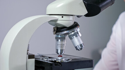 Concentrated lady employee with glasses takes blood drop from test tube with long pipette near microscope working in hospital close view