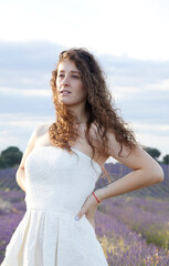 Fototapeta na wymiar Portrait of a young woman in the lavender fields of Brihuega, in Spain. She wears a white dress and her hair is loose and curly. Lifestyle. Beauty
