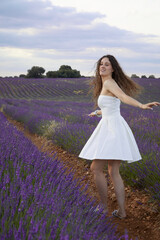 Photos of a young woman in the lavender fields of Brihuega, in Spain. She is spinning around in a white dress blowing in the wind. Lifestyle. Beauty