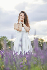 Fototapeta na wymiar American shot of a young woman in white dress in the lavender fields of Brihuega, in Spain. He is posing among plants, while walking.