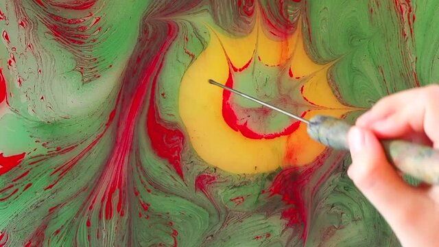 Thin stick in child's hand moves in water and makes star on its surface.
Process of creating drawings in ebru technique, painting on water, without a sketch.