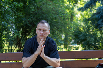 Naklejka na ściany i meble mature 50 year old handsome manly man with pensive look sits on a park bench