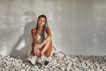 Woman in white summer clothing sitting leaning wall