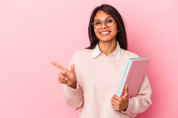 Young student latin woman isolated on pink background smiling and pointing aside, showing something at blank space.