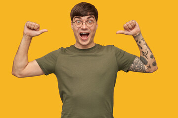 Indoor shot of young happy guy, looking directly into camera with widely opened eyes, point with...